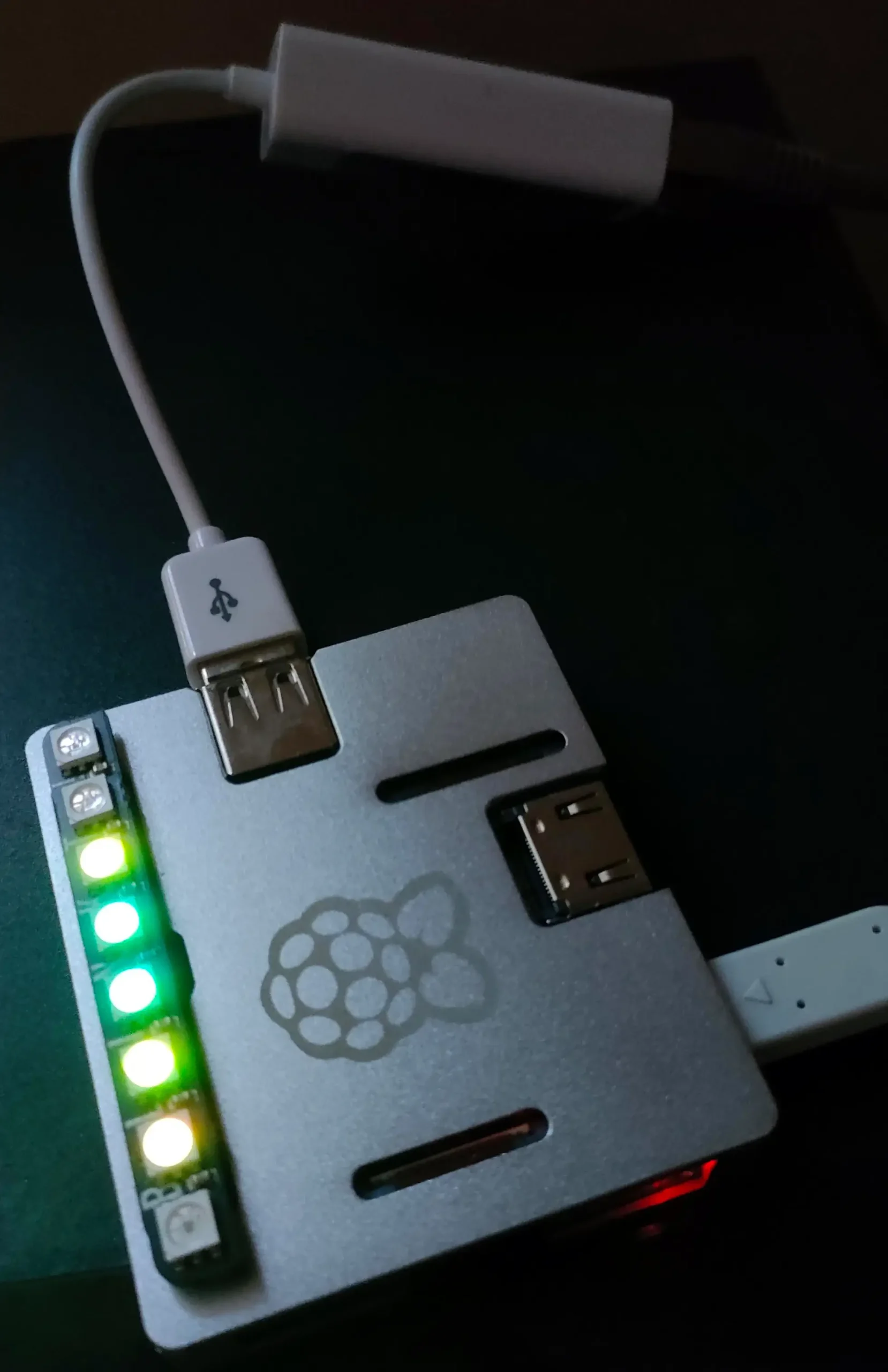 A Raspberry Pi Zero 2 W in a metal case with a Blinkt LED strip lit green and yellow as a VU meter, a USB ethernet adapter attached, and a USB stick of music plugged in.
